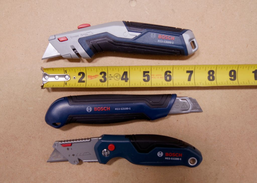 All three Bosch utility knives are laid out against a ruler showing that each knife is about 7 inches long.