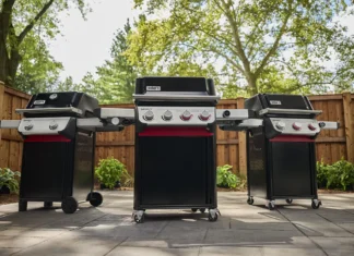 Three new 2025 Weber Spirit models side-by-side on a patio in a backyard on a warm spring day. From left to right is a two-burner, a four-burner, and three-burner 2025 Weber Spirit models