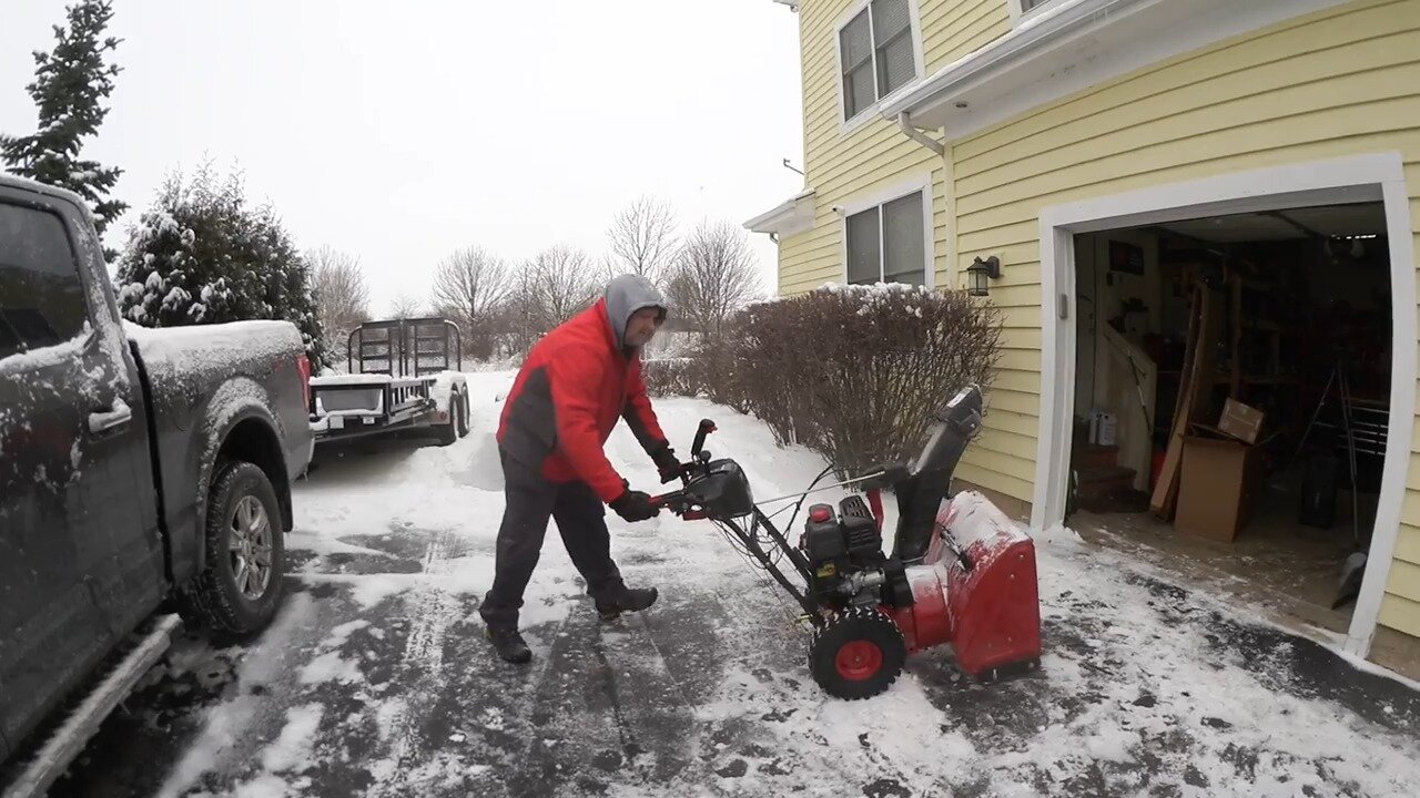 Craftsman snow blower throwing snow near a garage