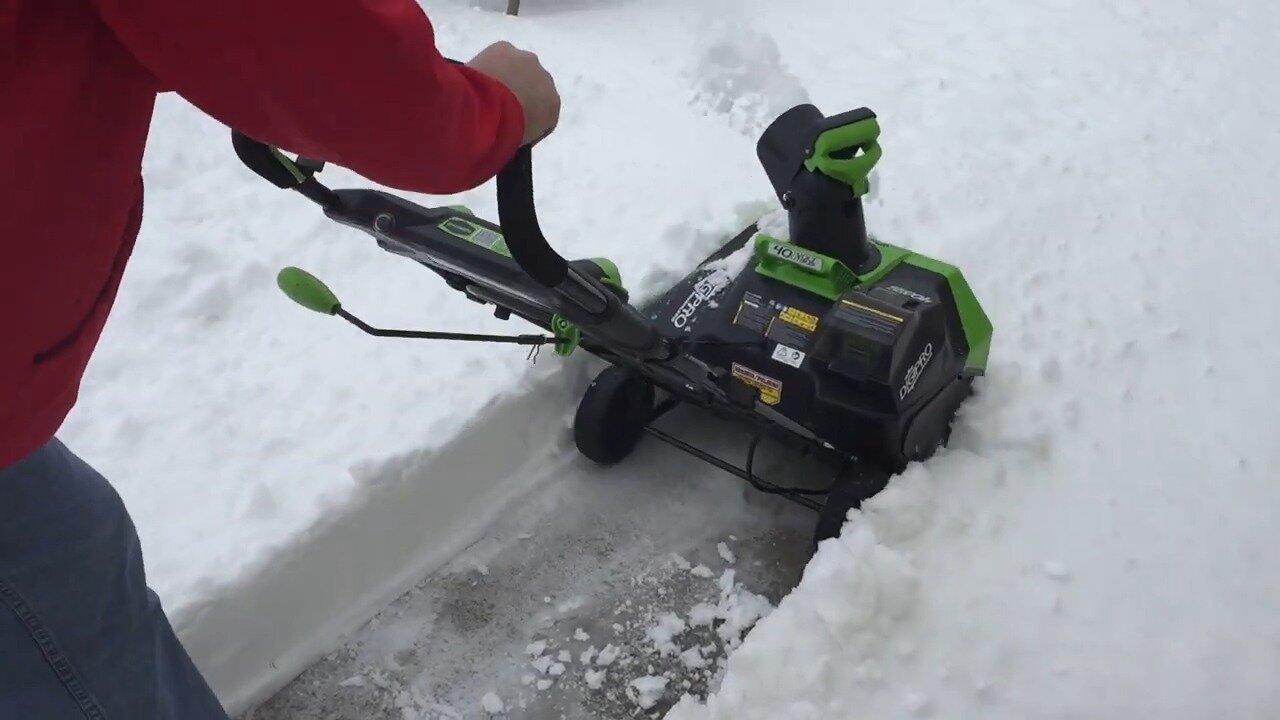 Greenworks 40V snow blower clearing a path along a wall of snow