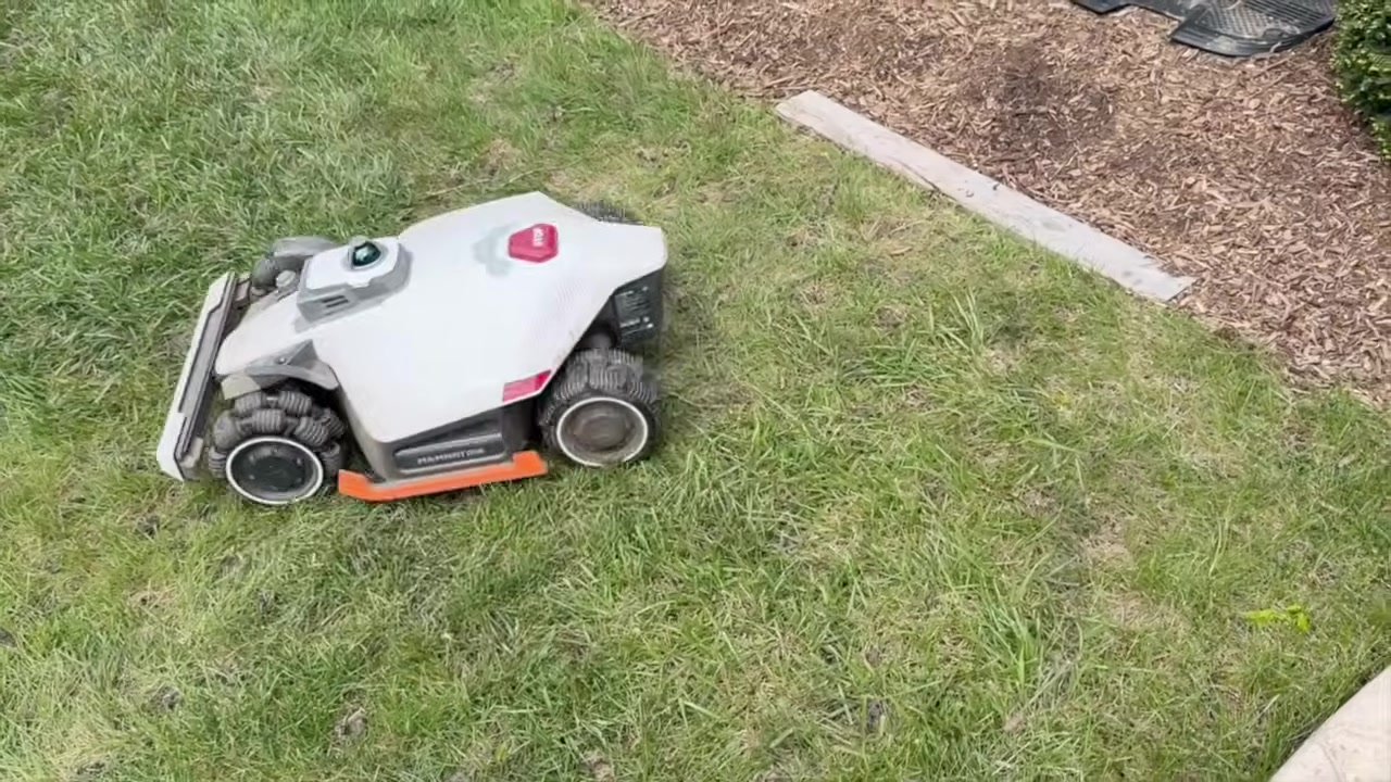 The LUBA 3 AWD robot mower working next to shrubs and a patio