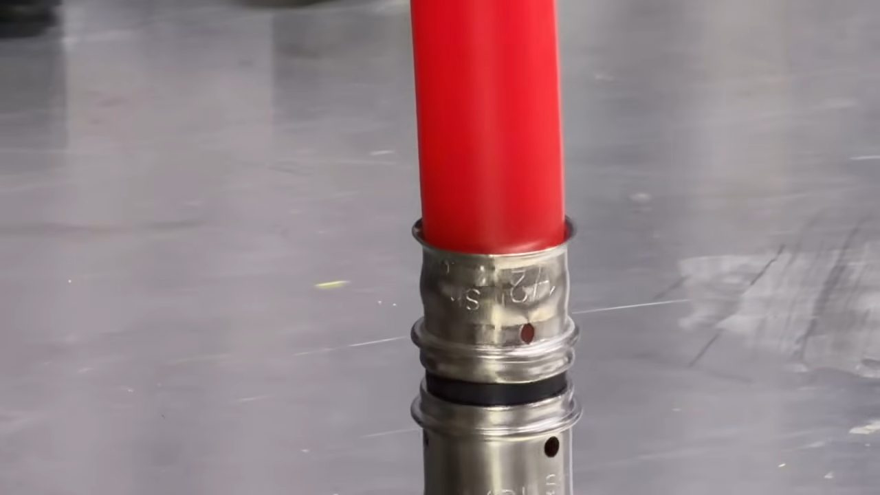 Pressed SharkBite PEX Press fitting on red PEX pipe, with the pipe showing through a viewing window in the stainless sleeve