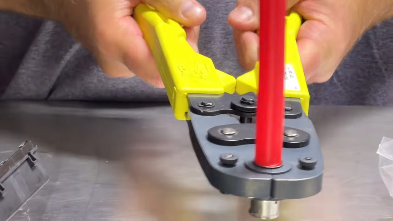 Squeezing the yellow handles of the SharkBite PEX press hand tool to press a fitting onto red PEX pipe